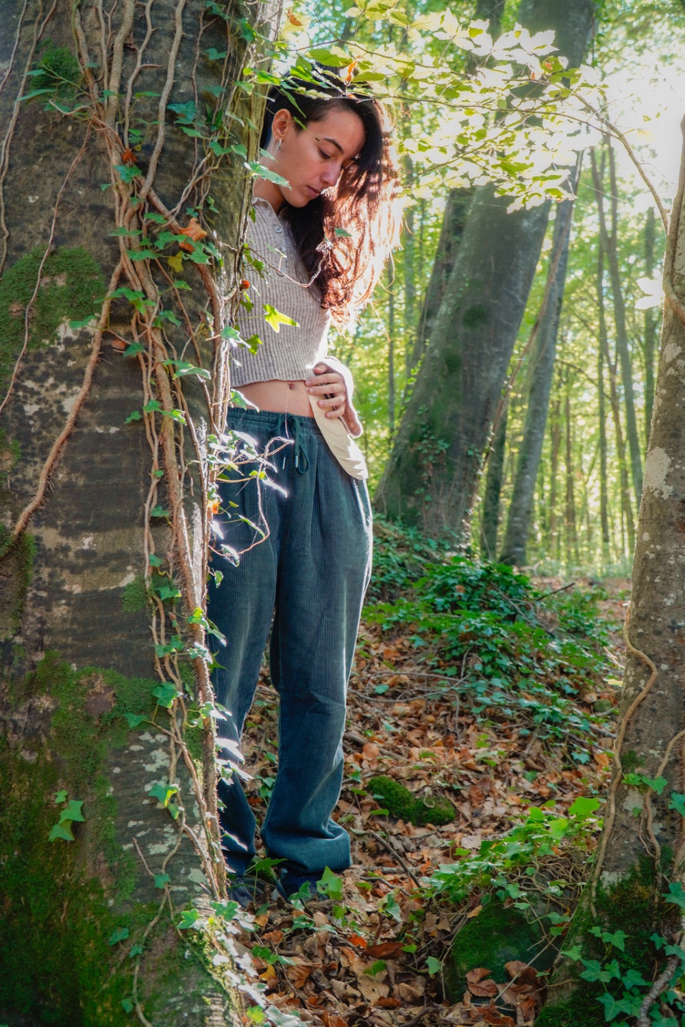 woman standing behind a tree in the forest holding the side of her belly in a nurturing manner, representing improved metabolic health