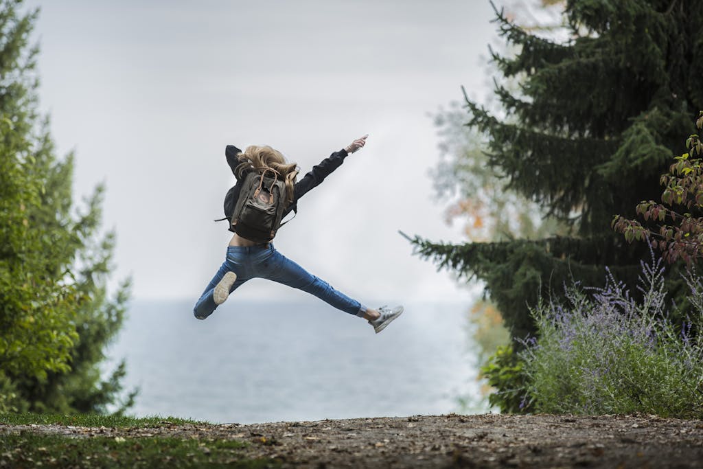 Energetic woman leaping in outdoor forest setting with lake view, showcasing freedom and joy, having improved her metabolic health and energy levels.
