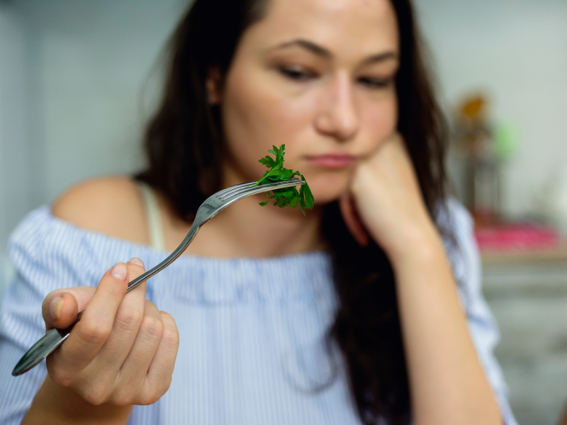 woman struggling with weight on a diet looking at some kale on a fork like she doesn't want to eat it