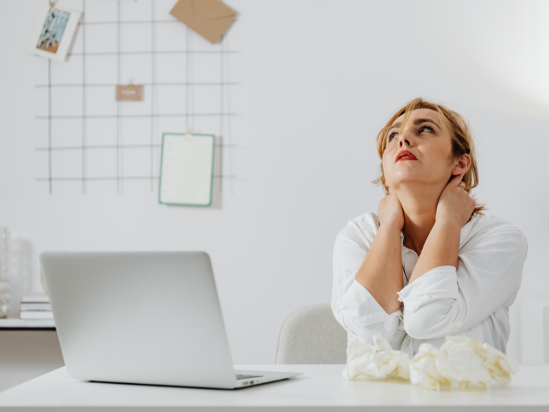 woman looking stressed holding neck sitting in front of laptop in her office