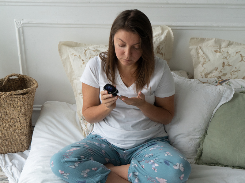woman looking tired in bed from lack of sleep and looking at her raised blood sugar on a monitor