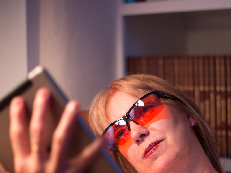 woman reading at night while wearing blue light blocking glasses to protect her circadian rhythms
