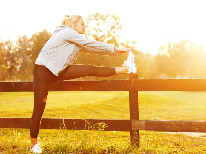 Woman stretching her leg on a fence outdoors under the sunlight