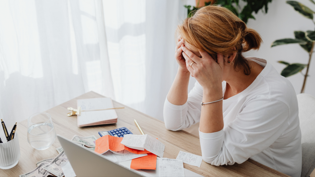 Stressed out woman sitting with her face in her hands with lots of work on her desk