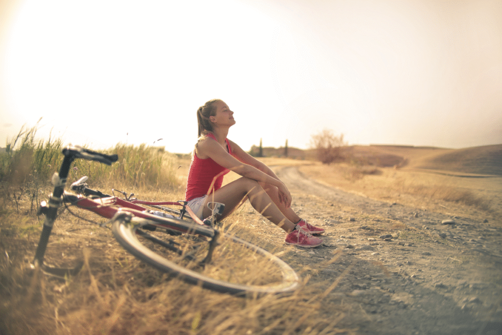 Vibrant woman sitting on the ground with her bike next to her with the sunrise in the background