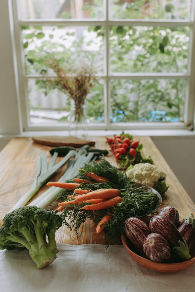 A selection of fresh vegetables on a rustic wooden table by a window.