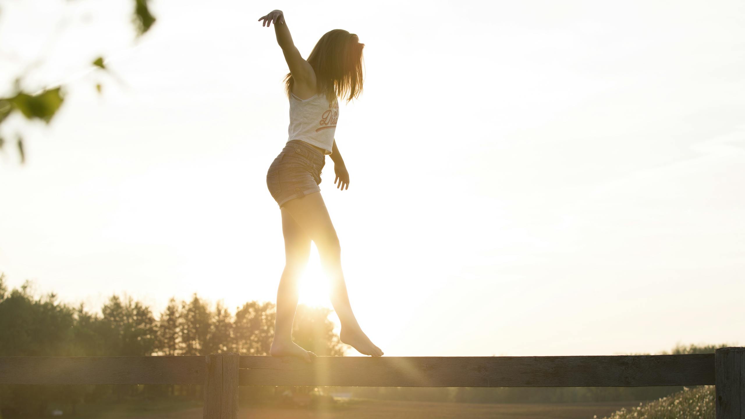 A young woman balancing on a fence during a serene sunrise, exuding freedom and joy.