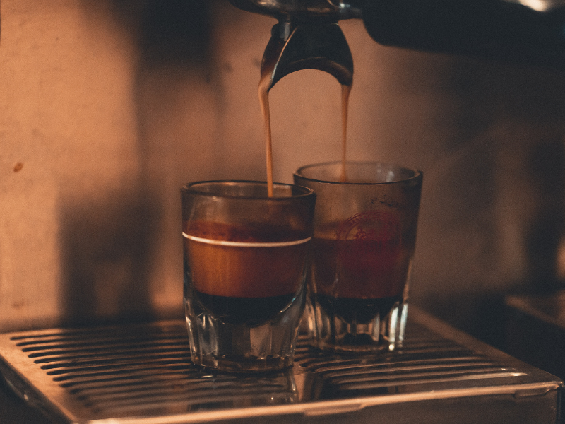 two cups of espresso being brewed by a coffee machine