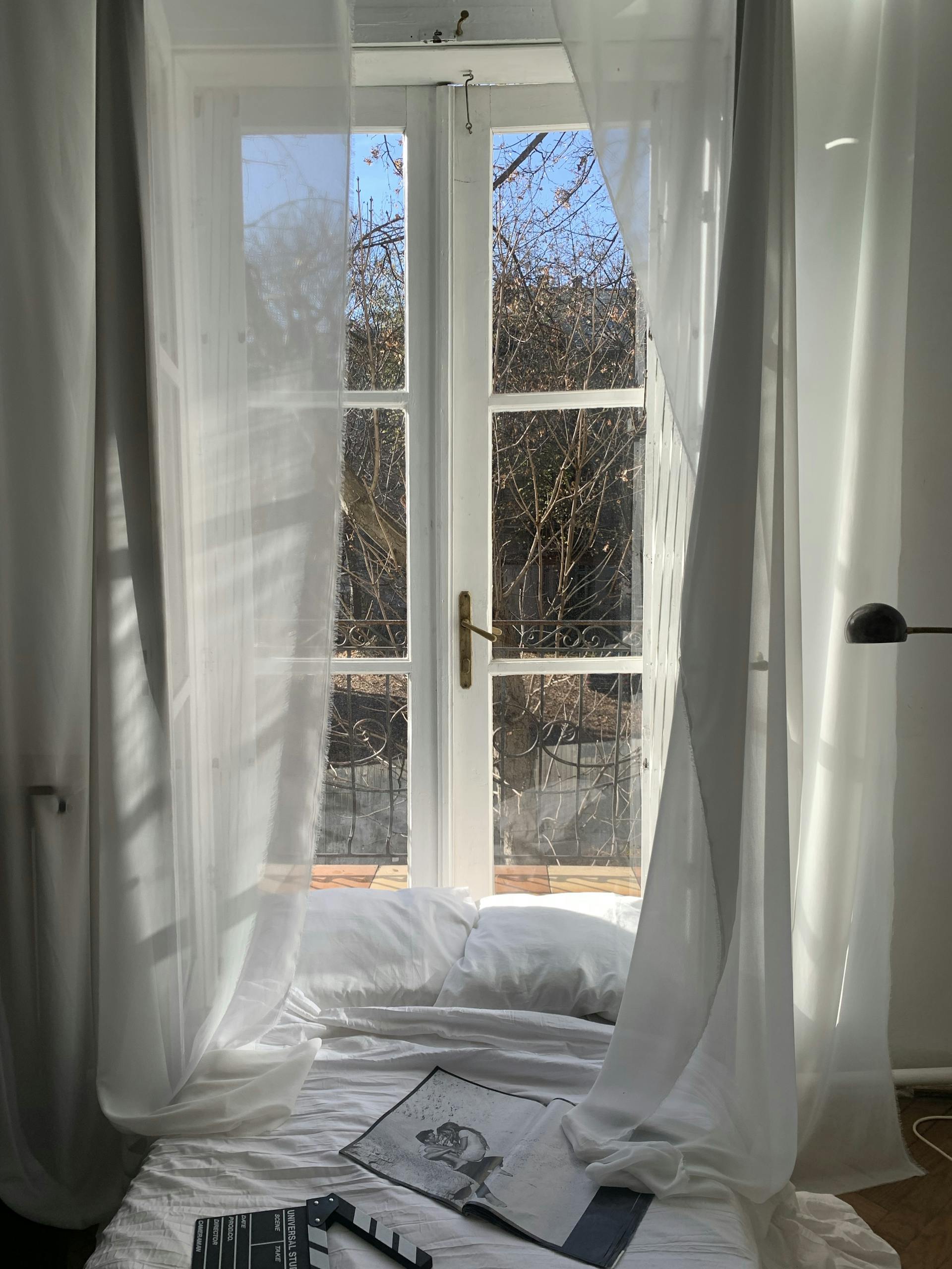 Bright bedroom with sunlight streaming through sheer curtains and an open window view.