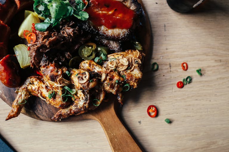 A top-view of roasted chicken with vegetables, sauce, and spices, served on a wooden board.